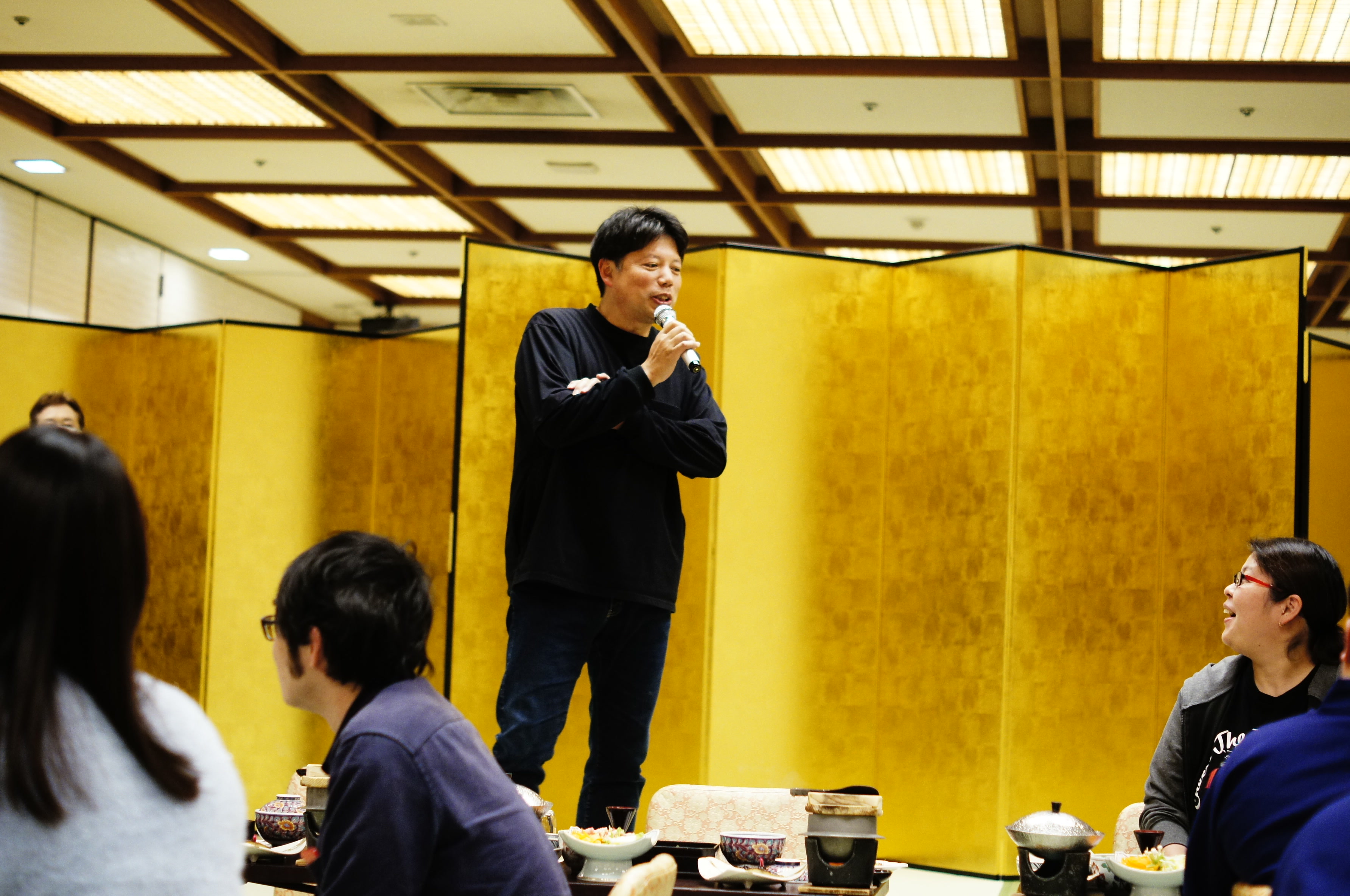 食事を囲む交流会で、マイクを手に話す登壇者と参加者